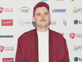 Mężczyzna w czerwonym ubraniu i czapce na tle logo Polskiej Ligi Esportowej.