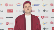 Mężczyzna w czerwonym ubraniu i czapce na tle logo Polskiej Ligi Esportowej.