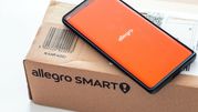 Na zdjęciu widoczny telefon z logo Allegro obok paczki Allegro Smart.