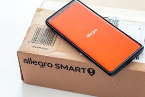 Na zdjęciu widoczny telefon z logo Allegro obok paczki Allegro Smart.