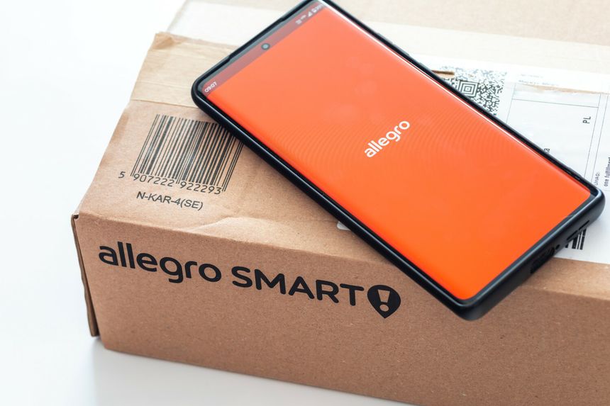 Na zdjęciu widoczny telefon z logo Allegro obok paczki Allegro Smart.