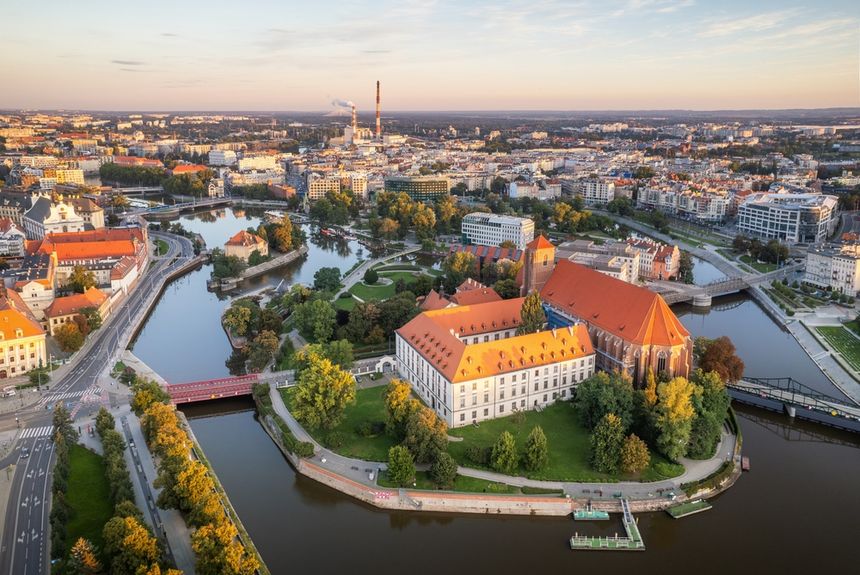 Widok na miasto z rzeką, mostami i zielenią, późne popołudnie, jasne niebo.
