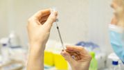 Osoba trzyma strzykawkę z igłą, przygotowując ją do zastrzyku w tle medycznym.