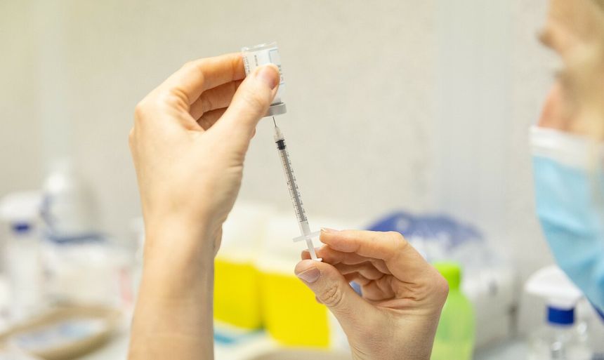 Osoba trzyma strzykawkę z igłą, przygotowując ją do zastrzyku w tle medycznym.