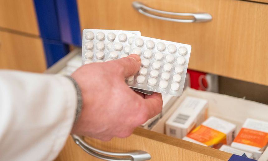 Ręka trzymająca opakowanie tabletek nad otwartą szufladą z lekami w aptece.