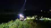 Na zdjęciu łódź na spokojnej wodzie w nocy, światła oraz osoby na brzegu.