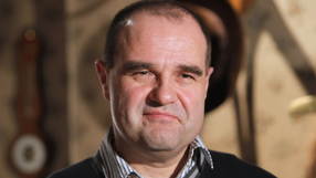 Mężczyzna w swetrze z widocznym uśmiechem, w tle jasne, przytulne wnętrze.