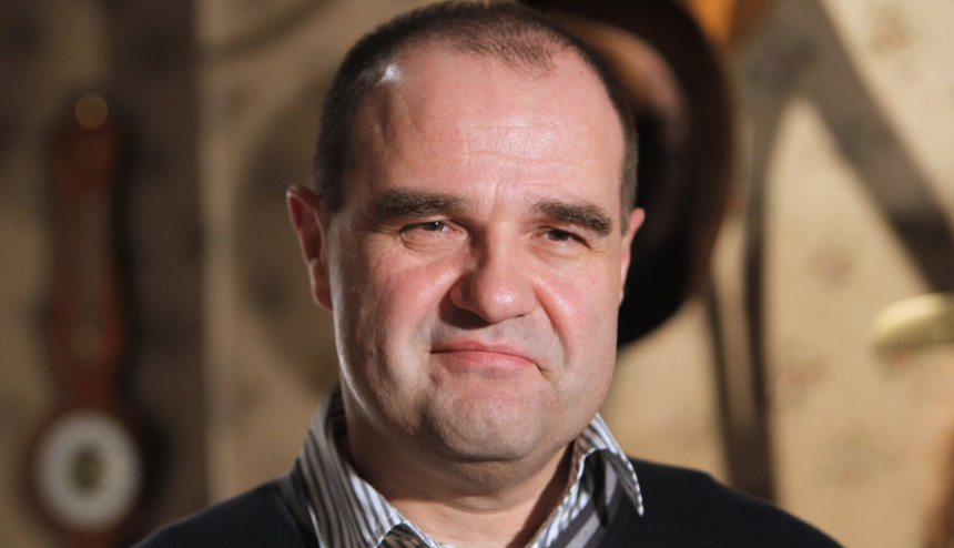 Mężczyzna w swetrze z widocznym uśmiechem, w tle jasne, przytulne wnętrze.