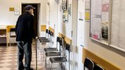 Mężczyzna w kapeluszu z laską stoi w korytarzu z krzesłami i zamkniętymi drzwiami.