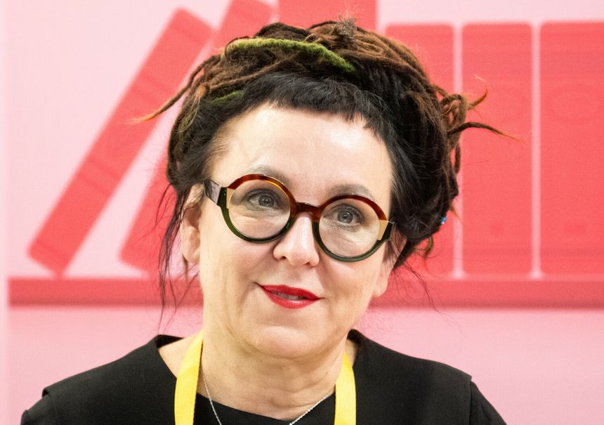 Kobieta z okrągłymi okularami, ciemnymi włosami w dredach, na tle różowych książek.