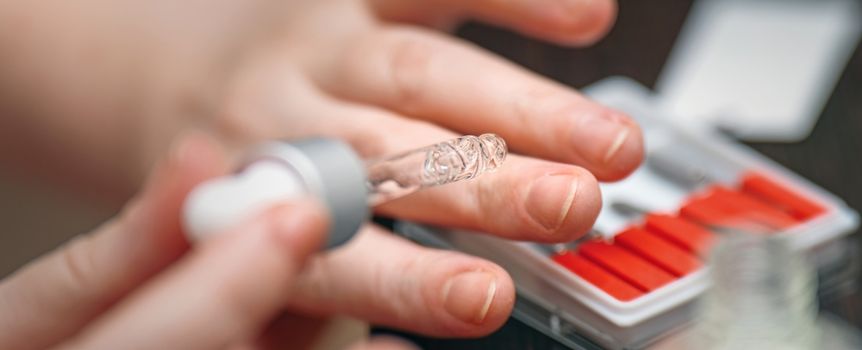 Ręka z pipetą aplikuje płyn na palec, obok pudełko z czerwonymi tabletkami.