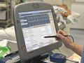 Urządzenie medyczne z wyświetlaczem, podłączone do pacjenta w szpitalu. Niedaleko leżą akcesoria.
