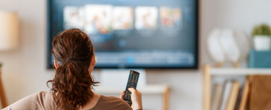 Kobieta siedzi na kanapie z pilotem w ręku, oglądając telewizję w jasnym salonie.