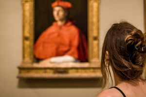 Kobieta stojąca przed portretem mężczyzny w czerwonym płaszczu i czapce w muzeum.