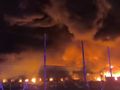 Widok płonącego budynku w otoczeniu dymu i ognia w ciemnej scenerii nocnej.