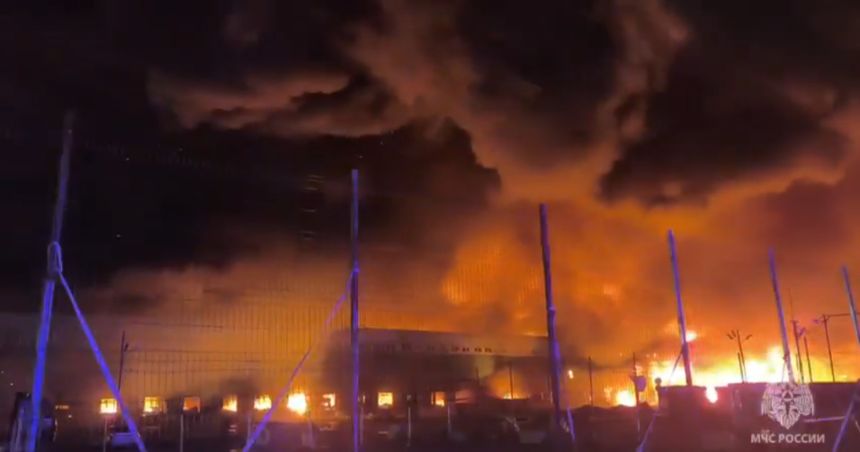 Widok płonącego budynku w otoczeniu dymu i ognia w ciemnej scenerii nocnej.