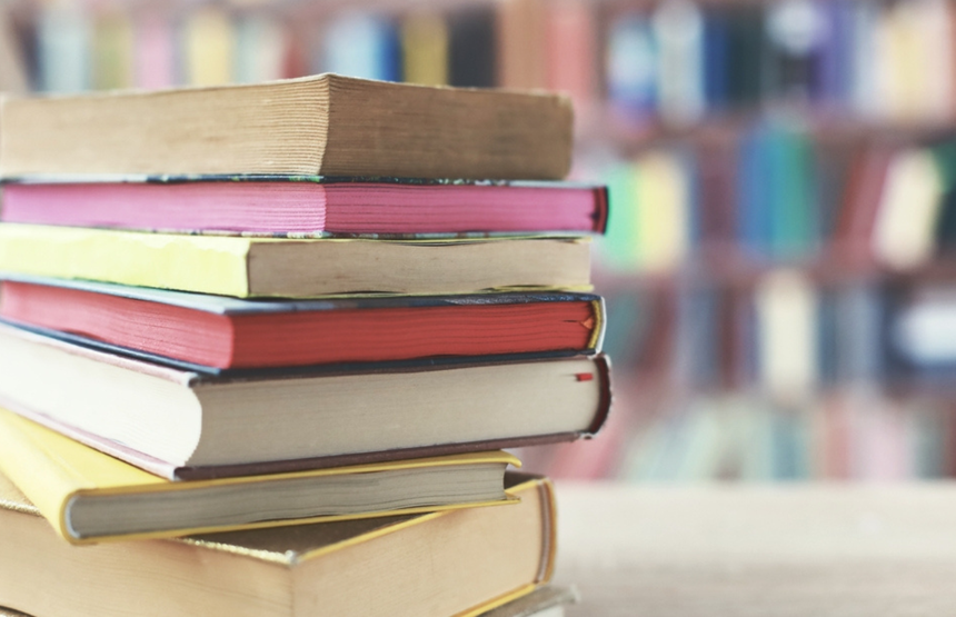 Stos książek w różnych kolorach na tle rozmytej biblioteki.