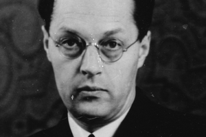 Mężczyzna w okularach, z poważnym wyrazem twarzy, ubrany w marynarkę, czarno-biała fotografia.