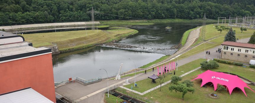 Widok na rzekę i tereny zielone, w tle budynki oraz różowe namioty. 