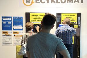 Trzy osoby korzystają z automatu do recyklingu, przystojąc przed wyświetlaczami informacyjnymi.