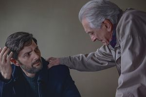 Na zdjęciu dwóch mężczyzn w rozmowie; starszy kładzie rękę na ramieniu młodszego.