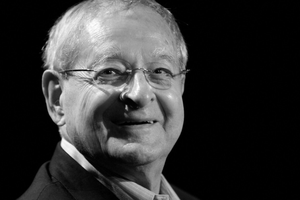 Osoba w okularach, uśmiechająca się, ciemne tło, portret w odcieniach czerni i bieli.