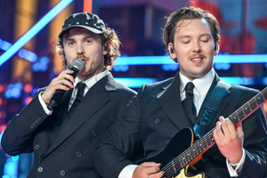 Na scenie dwóch mężczyzn w eleganckich garniturach, jeden śpiewa, drugi gra na gitarze.