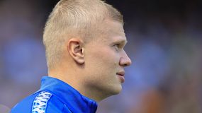 Erling Haaland w niebieskiej bluzie oglądający wydarzenie sportowe, widok z profilu.