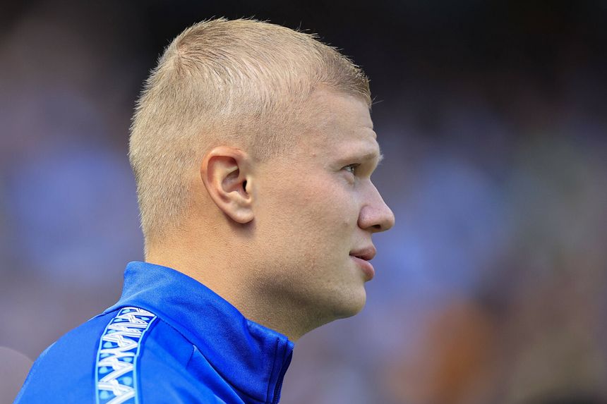 Erling Haaland w niebieskiej bluzie oglądający wydarzenie sportowe, widok z profilu.