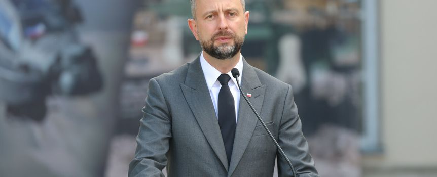 Na zdjęciu mężczyzna w garniturze przy mównicy, wyraża uwagę podczas przemówienia.