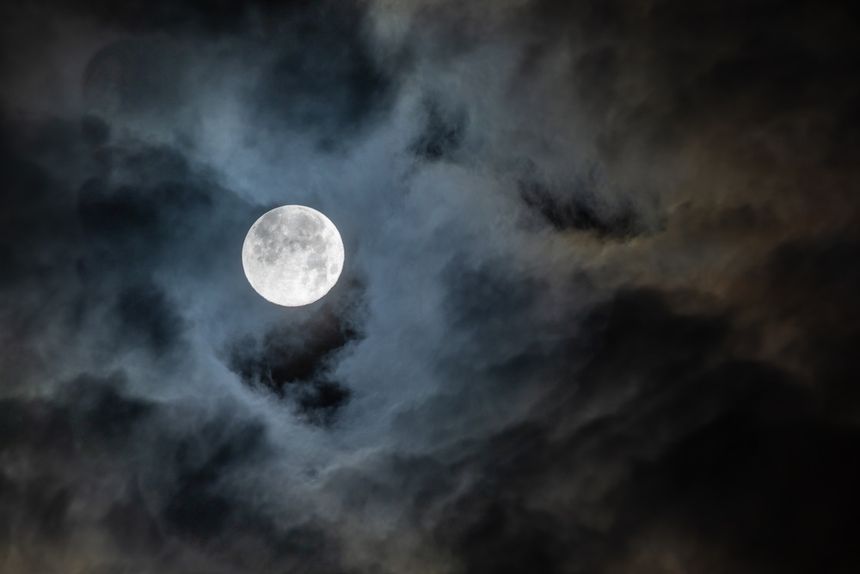 Pełnia Księżyca na tle ciemnych chmur, tworzących tajemniczy klimat nocnego nieba.