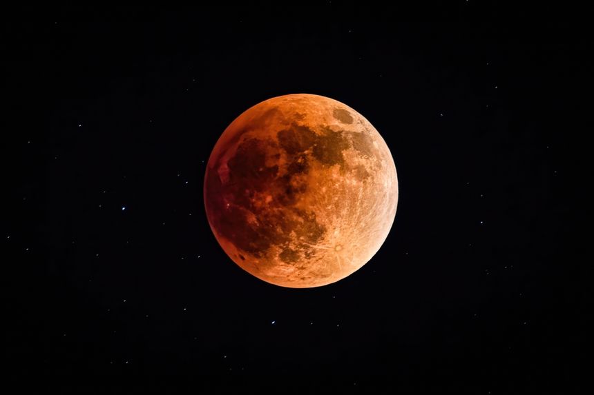 Czerwony Księżyc na tle gwiazd, nocne niebo, jasne i ciemne obszary na powierzchni.
