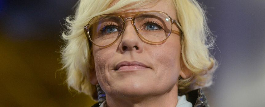 Kobieta z krótkimi blond włosami i dużymi okularami, patrzy w górę.