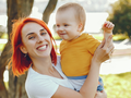 Rudowłosa mama nosząca na rękach uśmiechniętego małego chłopca w żółtej koszulce