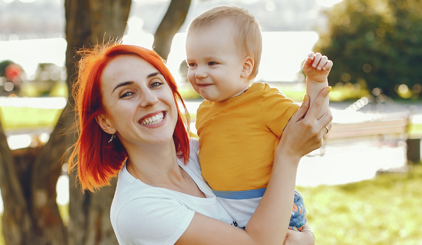 Rudowłosa mama nosząca na rękach uśmiechniętego małego chłopca w żółtej koszulce