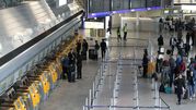 Widok na wnętrze lotniska z linią odprawy i pasażerami oraz tablicą odlotów.