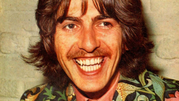 George Harrison. Mężczyzna z długimi, kręconymi włosami, uśmiechnięty, w kolorowej marynarce.