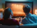 Para siedzi na kanapie, oglądając telewizję i jedząc popcorn w przytulnym wnętrzu.