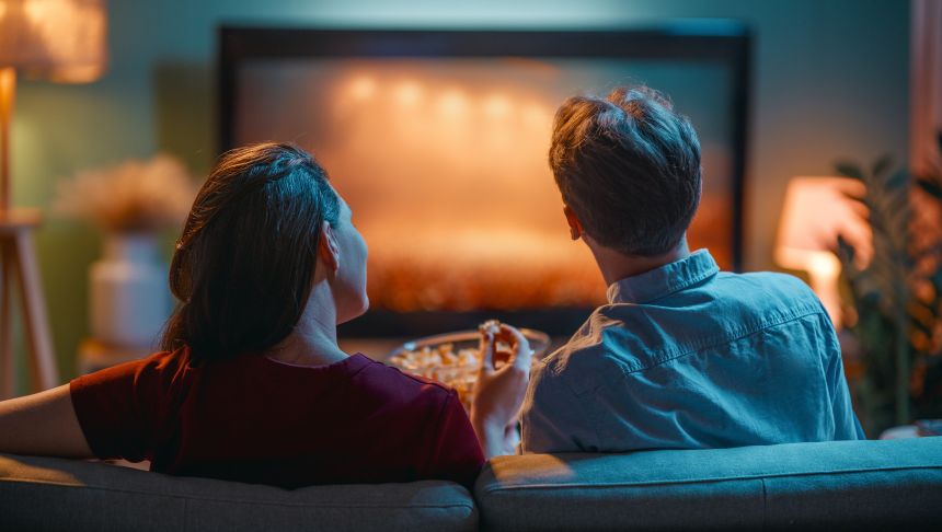 Para siedzi na kanapie, oglądając telewizję i jedząc popcorn w przytulnym wnętrzu.