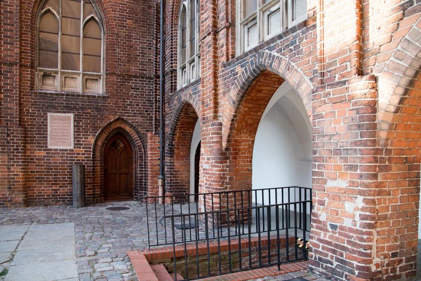Zdjęcie przedstawia ceglaną architekturę z łukami i drewnianymi drzwiami.
