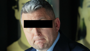 Mężczyzna w garniturze z szarym włosami, patrzy w kamerę z poważnym wyrazem twarzy.