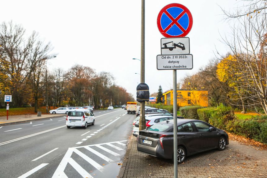 Widok ulicy z zakazem parkowania, samochody zaparkowane, drzewo i znaki drogowe.
