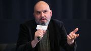 Mężczyzna w ciemnym garniturze, trzyma mikrofon, gestykulując podczas dyskusji.