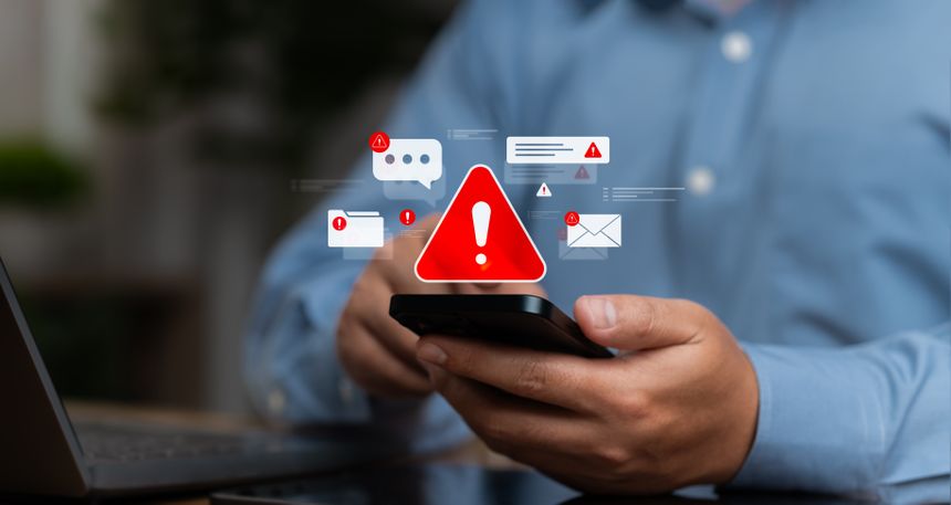Mężczyzna trzyma telefon, na którym wyświetlają się powiadomienia z symbolami ostrzeżeń.