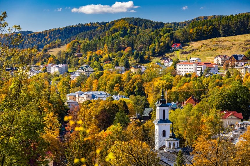 Widok na malownicze miasteczko w górach, otoczone kolorowymi drzewami w jesieni.