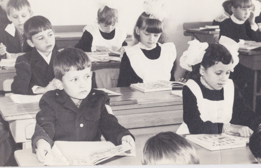 Czarno-białe zdjęcie dzieci w szkolnych ławkach, uczących się z podręczników.