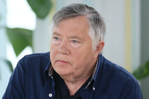 Mężczyzna w granatowej koszuli, z szarymi włosami, siedzi w jasnym pomieszczeniu.