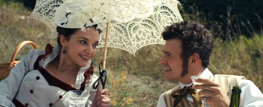 Mężczyzna i kobieta na pikniku, trzymają w rękach kieliszki, uśmiechają się, parasol nad głowami.