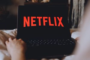 Na zdjęciu laptop z wyświetlonym logo Netflix na czarnym tle, ręka w zasięgu ekranu.