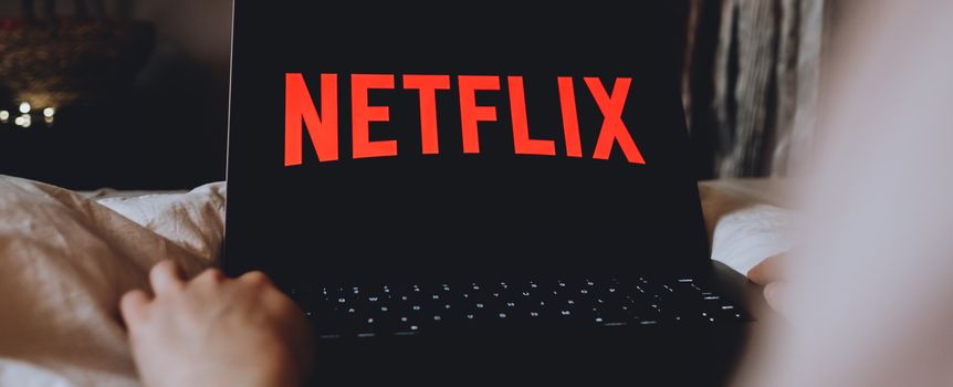 Na zdjęciu laptop z wyświetlonym logo Netflix na czarnym tle, ręka w zasięgu ekranu.